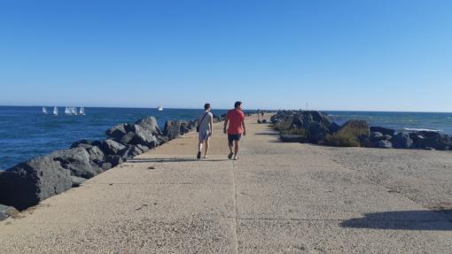 Dos hombres caminan por el espigón hacia el faro